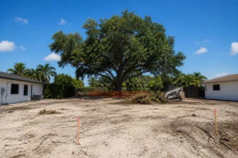 Infill teardown lot in Pompano Beach cleared to pale sand, one grand live oak preserved behind orange protection fencing